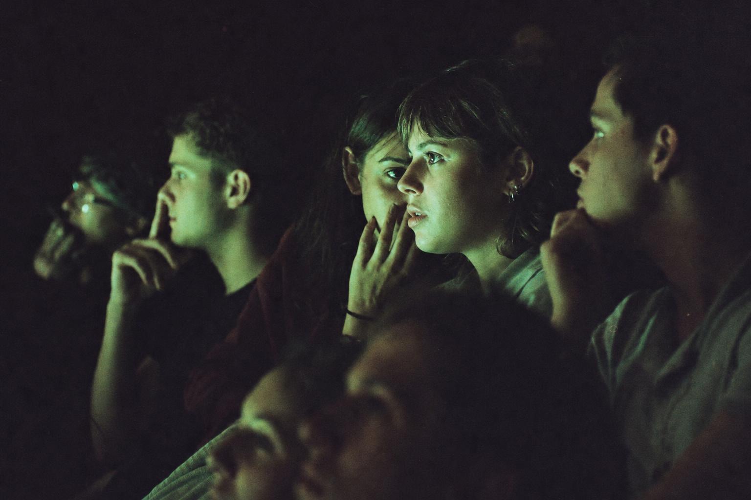 Audience faces lit green by a projected terminal feed