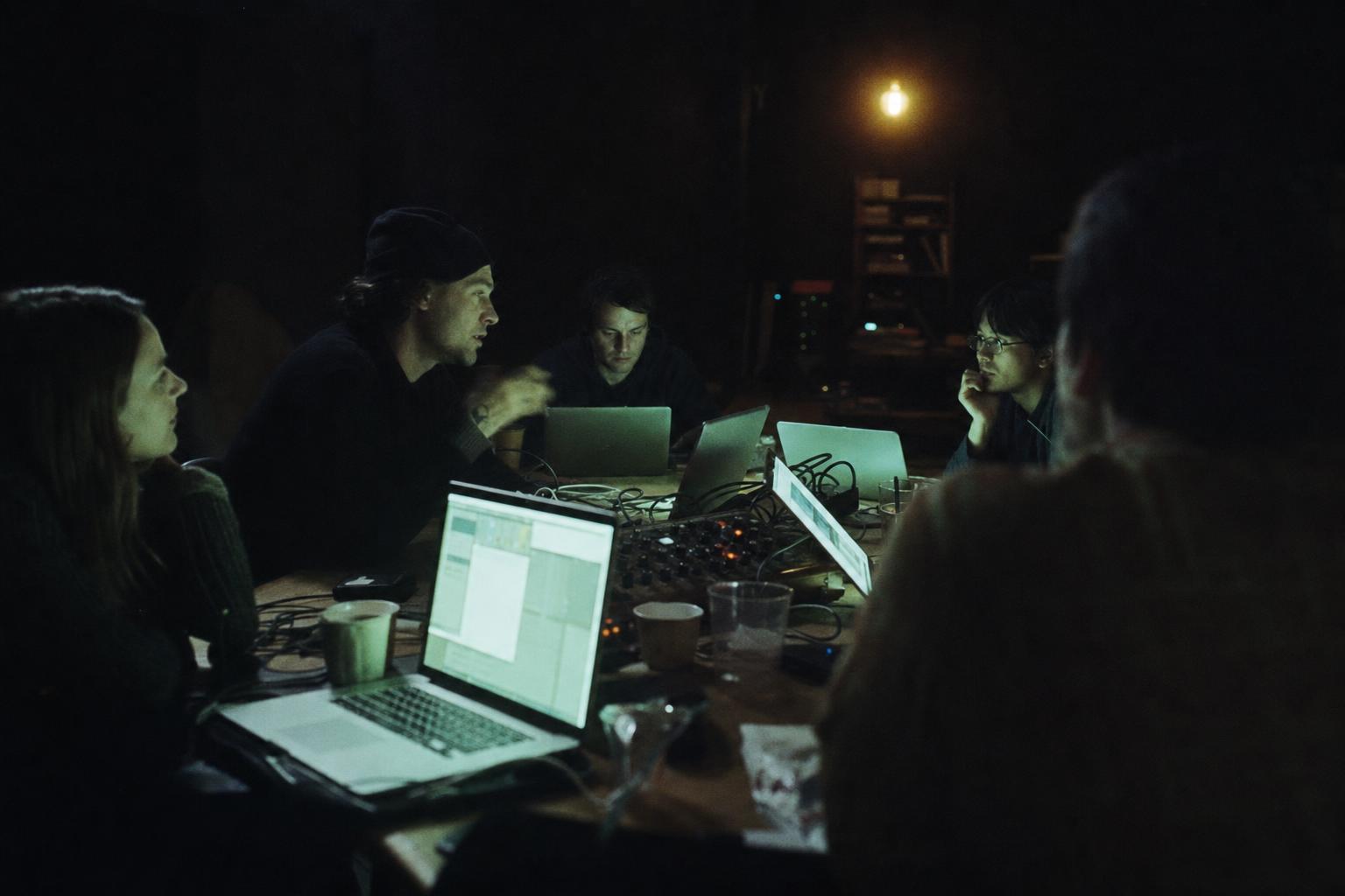 Faces around one table at night, lit by their screens